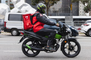 Entregador dirigindo moto com bag do iFood.
