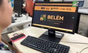 Computador com o site da Prefeitura de Belém aberto enquanto uma mulher olha.