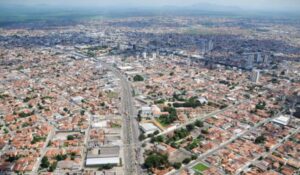 Vista aérea de uma cidade com ruas largas, casas de telhados vermelhos e prédios mais altos concentrados ao fundo.