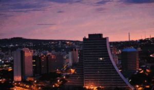 Vista panorâmica de Belo Horizonte ao entardecer, com prédios iluminados e céu em tons de roxo e rosa.