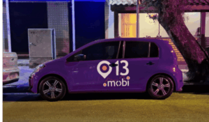 Carro roxo estacionado na rua à noite, com o logotipo “013 mobi” estampado na lateral, iluminado por luzes coloridas.