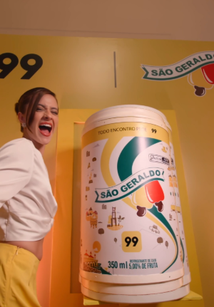 Mulher animada ao lado de lata temática de refrigerante da São Geraldo em parceria com a 99.