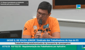 Homem de óculos e camiseta laranja fala ao microfone durante audiência pública na Câmara dos Deputados.