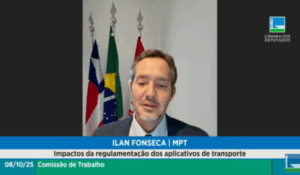 Homem fala por videoconferência durante audiência pública da Câmara dos Deputados, com bandeiras do Brasil e da Bahia ao fundo.