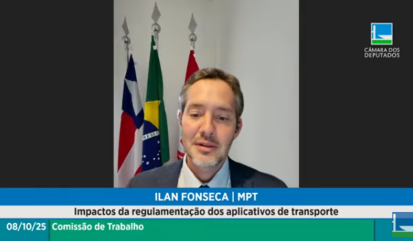 Homem fala por videoconferência durante audiência pública da Câmara dos Deputados, com bandeiras do Brasil e da Bahia ao fundo.