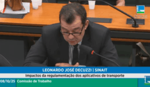 Homem de terno escuro e óculos lê documento ao microfone durante audiência pública na Câmara dos Deputados.