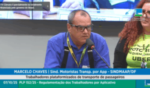 Homem de óculos e camisa azul fala ao microfone durante audiência pública na Câmara dos Deputados, ao lado de outros participantes.