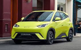 Carro elétrico compacto na cor verde-limão estacionado em rua urbana próxima a prédios comerciais.