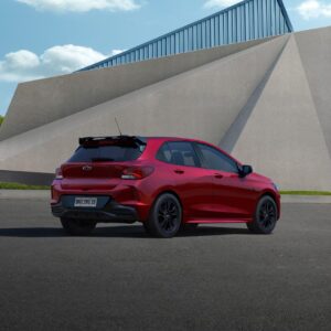 Carro hatch vermelho estacionado em área urbana moderna com estrutura arquitetônica ao fundo.