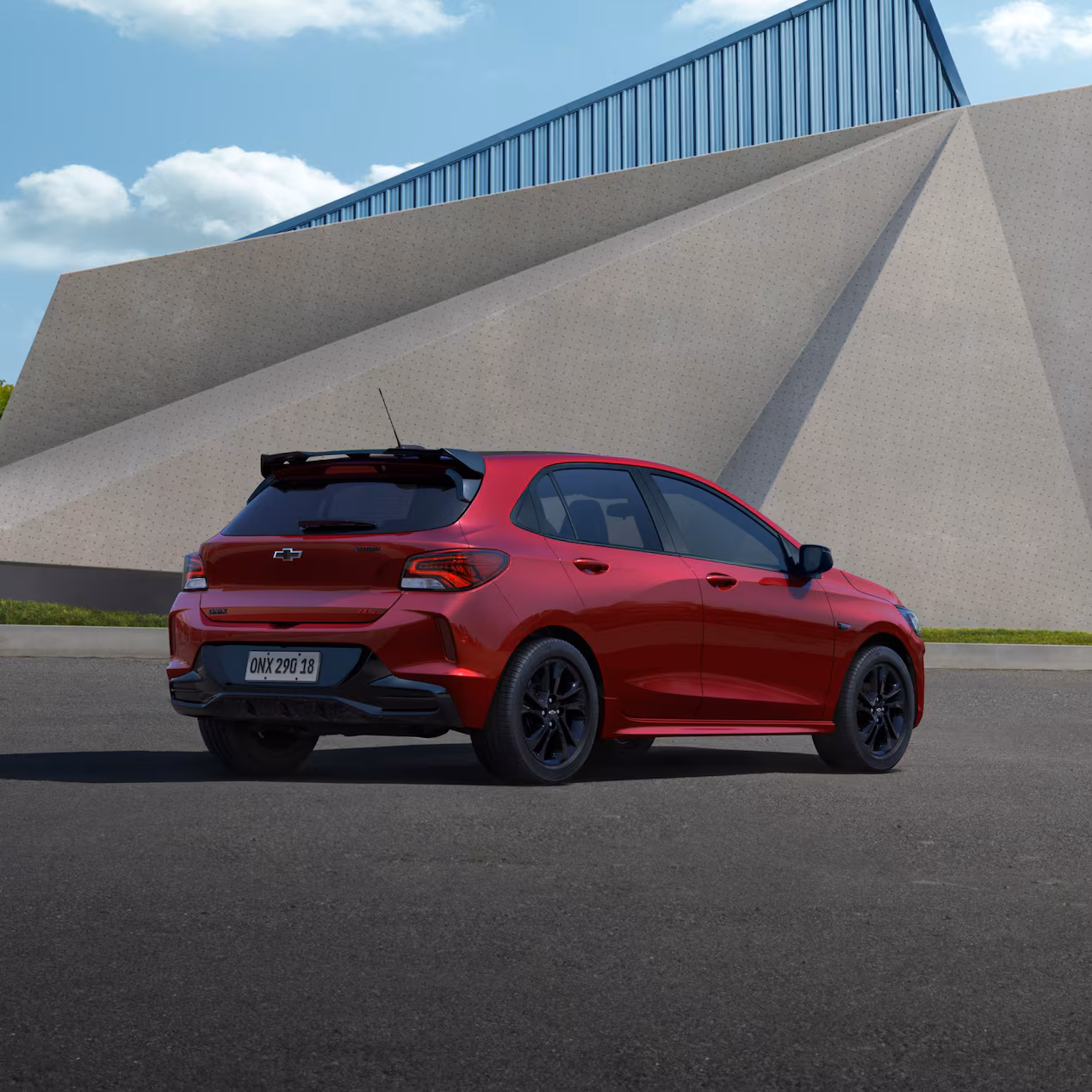 Carro hatch vermelho estacionado em área urbana moderna com estrutura arquitetônica ao fundo.