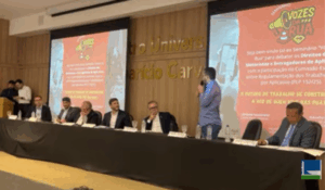 Painel de debate com vários participantes sentados à mesa em auditório, durante o seminário “Vozes da Rua”, que discute os direitos de motoristas e entregadores de aplicativo.