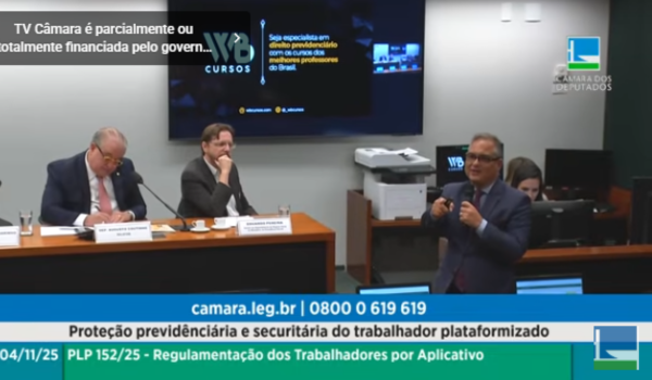 Cena de audiência pública na Câmara dos Deputados sobre a proteção previdenciária e securitária do trabalhador plataformizado. À mesa, dois homens estão sentados, um deles falando ao microfone, enquanto outro homem de terno fala em pé, gesticulando.