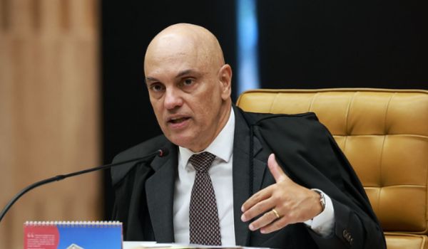 Ministro do Supremo Tribunal Federal fala durante sessão, sentado em uma cadeira de couro, usando terno e toga, com a mão levantada e um microfone à frente.