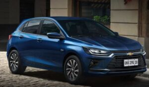 Carro Chevrolet Onix azul estacionado em uma rua de paralelepípedos em frente a um prédio antigo.