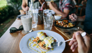 Prato com ovos pochê sobre torrada em mesa de restaurante, com pessoas ao fundo.
