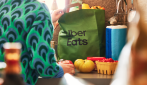Pessoa retira sacola verde do Uber Eats com mantimentos sobre bancada de cozinha.
