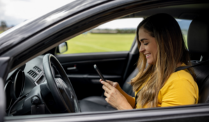 Mulher sentada no banco do motorista usando o celular enquanto está dentro de um carro.