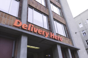 Fachada de prédio comercial com letreiro vermelho “Delivery Hero” acima da entrada