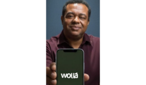 Homem sorridente segura um smartphone exibindo o aplicativo Wolla na tela, em fundo neutro.