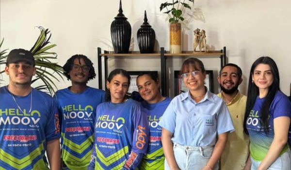 Grupo de seis pessoas usando camisetas personalizadas da Hello Moov em ambiente interno com estante ao fundo.
