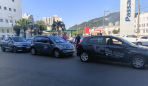 Carros adesivados da Via Car estacionados em fila em área urbana, com prédios e morro ao fundo.