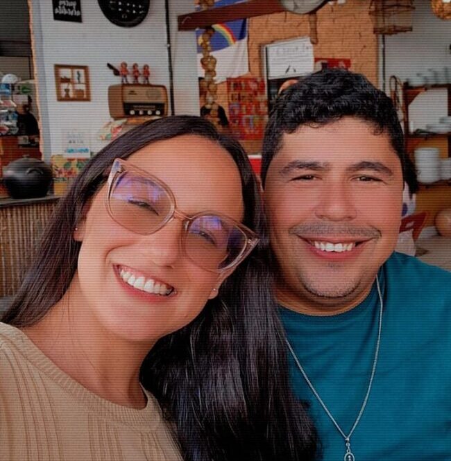 Casal sorrindo em ambiente interno com decoração rústica e iluminação aconchegante.