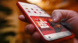 Pessoa segurando um smartphone com o aplicativo iFood aberto na tela, exibindo a interface da plataforma de delivery.