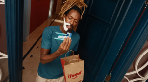 Entregador do iFood segura produtos de higiene pessoal e uma sacola da marca em uma porta residencial durante entrega.