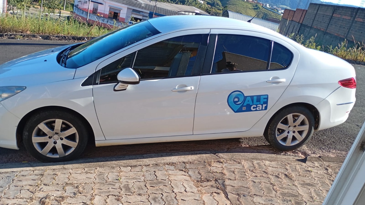 Carro branco estacionado junto ao meio-fio, visto de lado, com identificação ALF car na porta traseira.