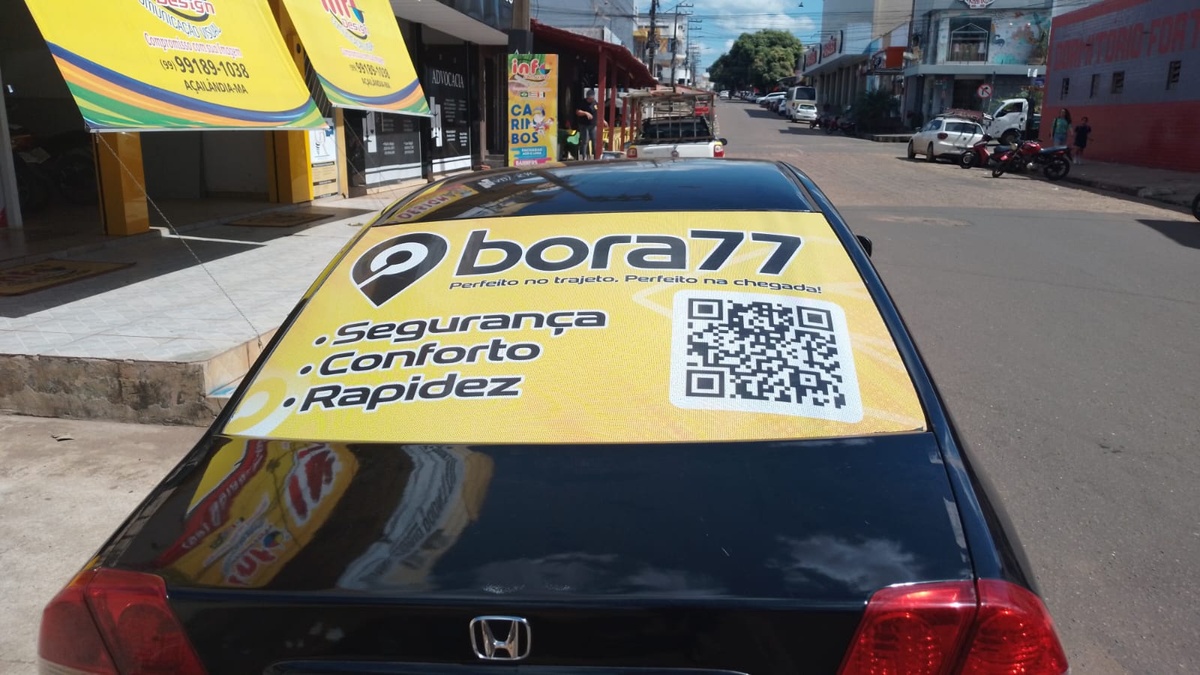Traseira de carro preto com anúncio amarelo da Bora77 no vidro, estacionado em uma rua comercial.