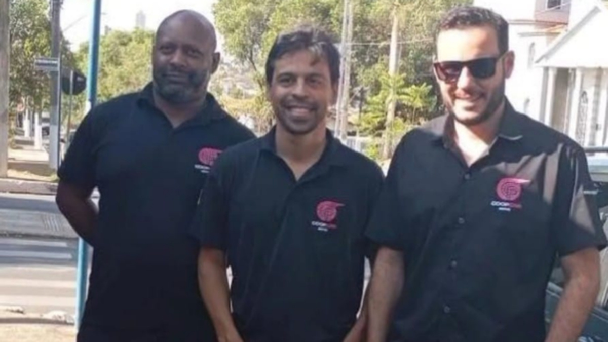 Três homens usando camisas pretas com identificação da Coopcar posam juntos em uma área externa.