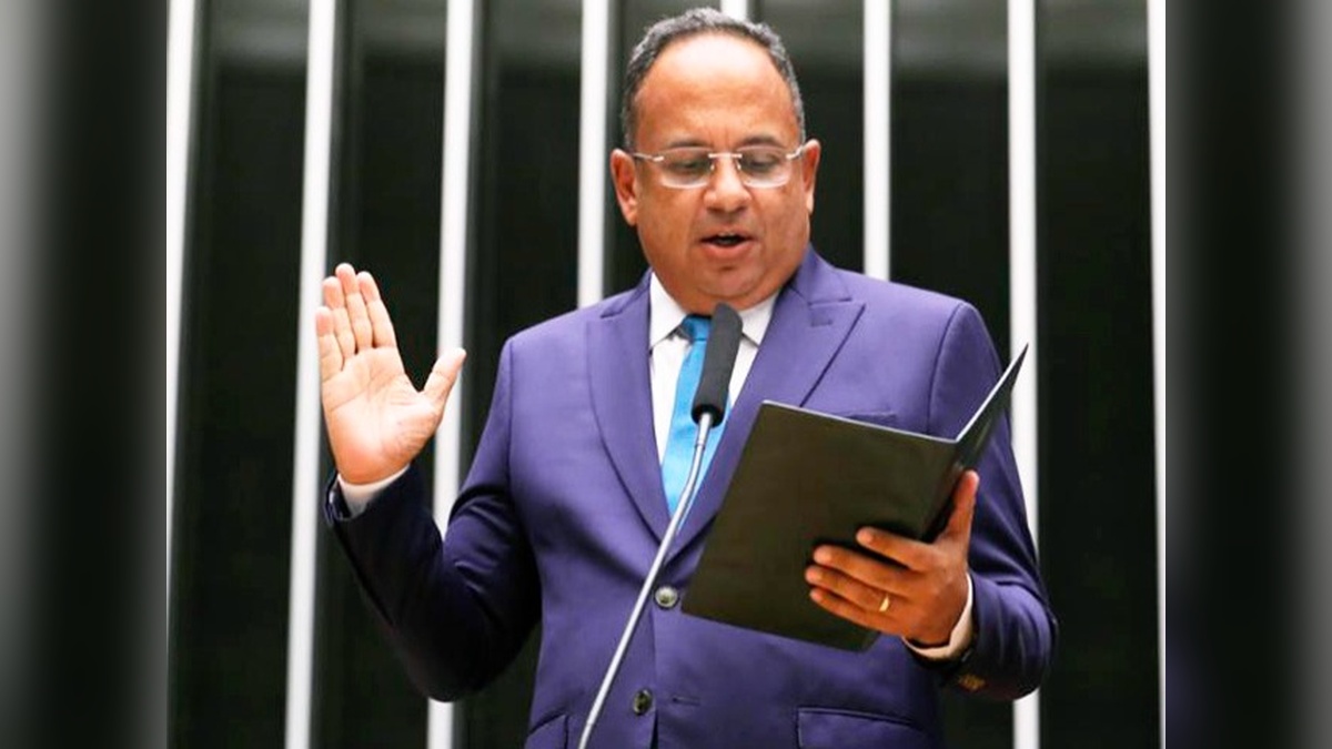 Homem de terno azul lê um documento diante de um microfone, com uma das mãos levantada.