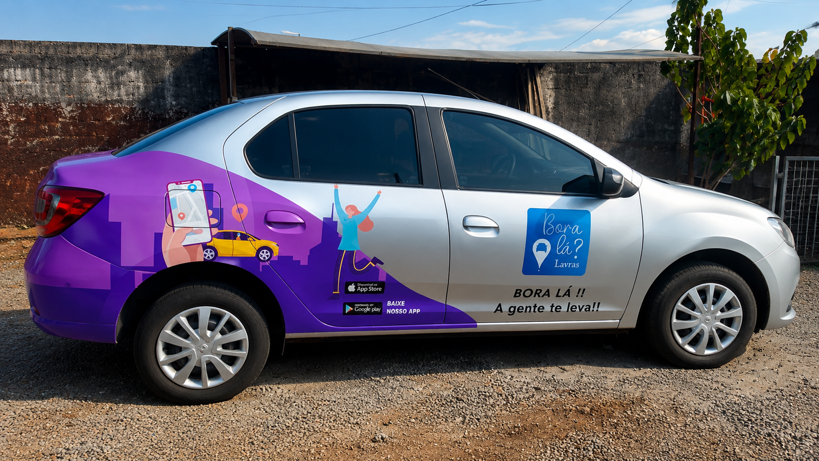 Vista lateral de um carro prata adesivado com a identidade visual do aplicativo Bora Lá Lavras. O adesivo em tons de roxo e azul mostra ilustrações de um celular com mapa, um carro e uma pessoa comemorando, além do logotipo da marca, a frase "Bora lá!! A gente te leva!!" e ícones para download do aplicativo.