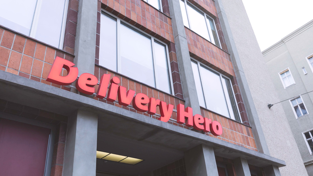 Fachada de edifício com janelas amplas e letreiro vermelho da Delivery Hero sobre a entrada.