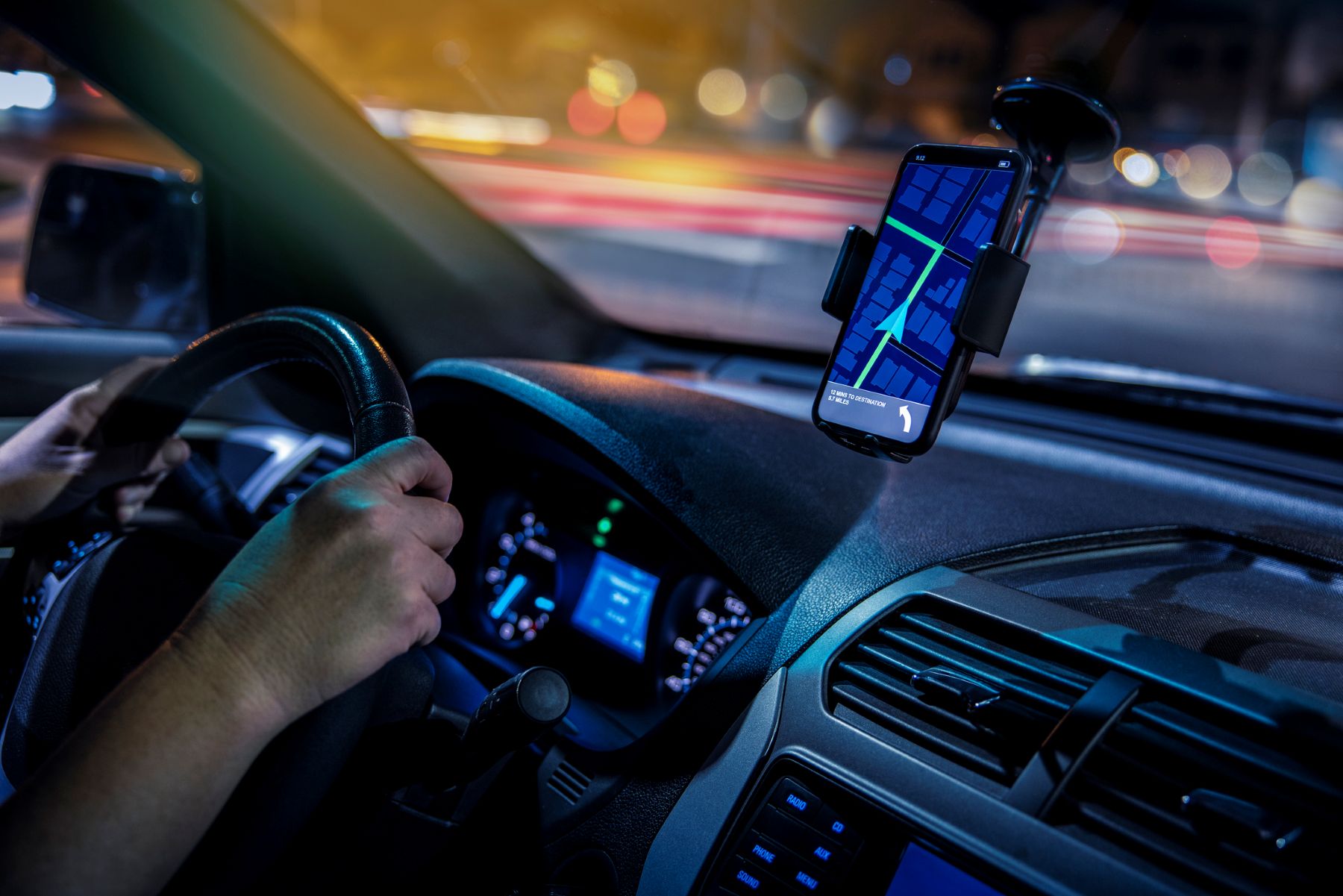Motorista conduz veículo enquanto utiliza aplicativo de navegação em smartphone fixado no painel, representando taxistas e motoristas de aplicativo.