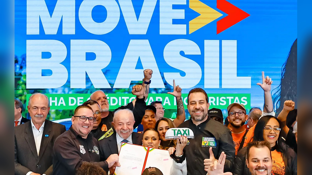 Grupo de pessoas posa diante de um painel do Move Brasil; participantes seguram um documento e uma placa com a palavra “Táxi”.