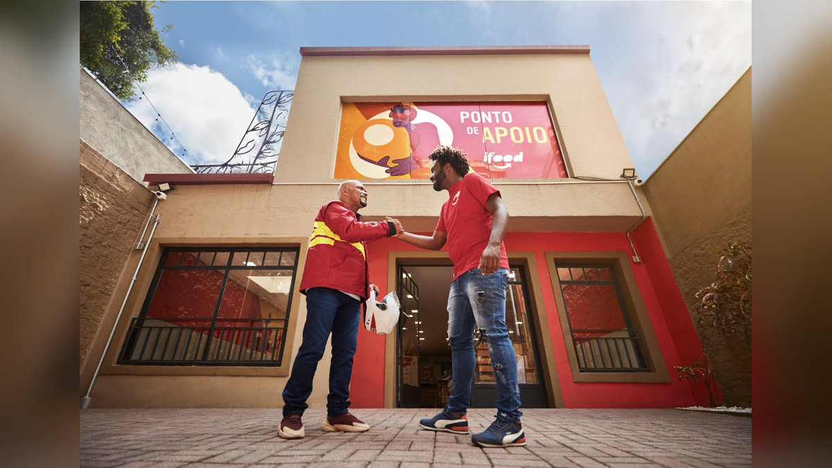 Dois homens se cumprimentam diante da fachada de um Ponto de Apoio do iFood.