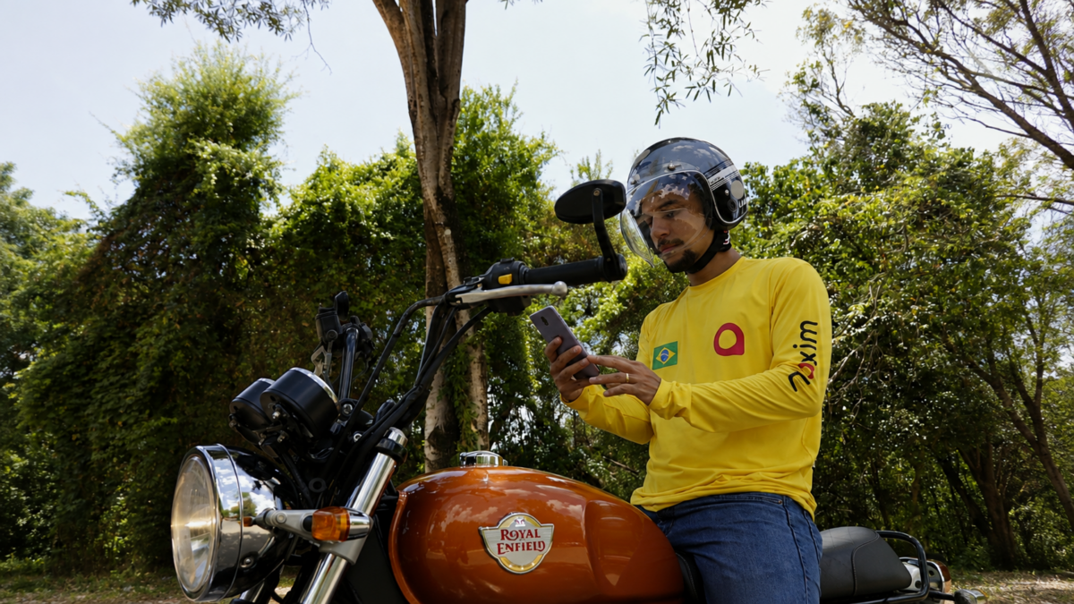 Motorista parceiro da Maxim consulta o celular ao lado de uma motocicleta.