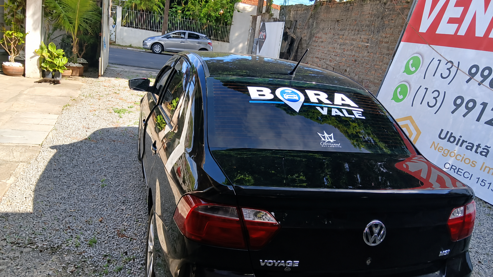 Carro Volkswagen Voyage preto estacionado em área externa, visto pela traseira, com adesivo “Bora Vale” no vidro traseiro.