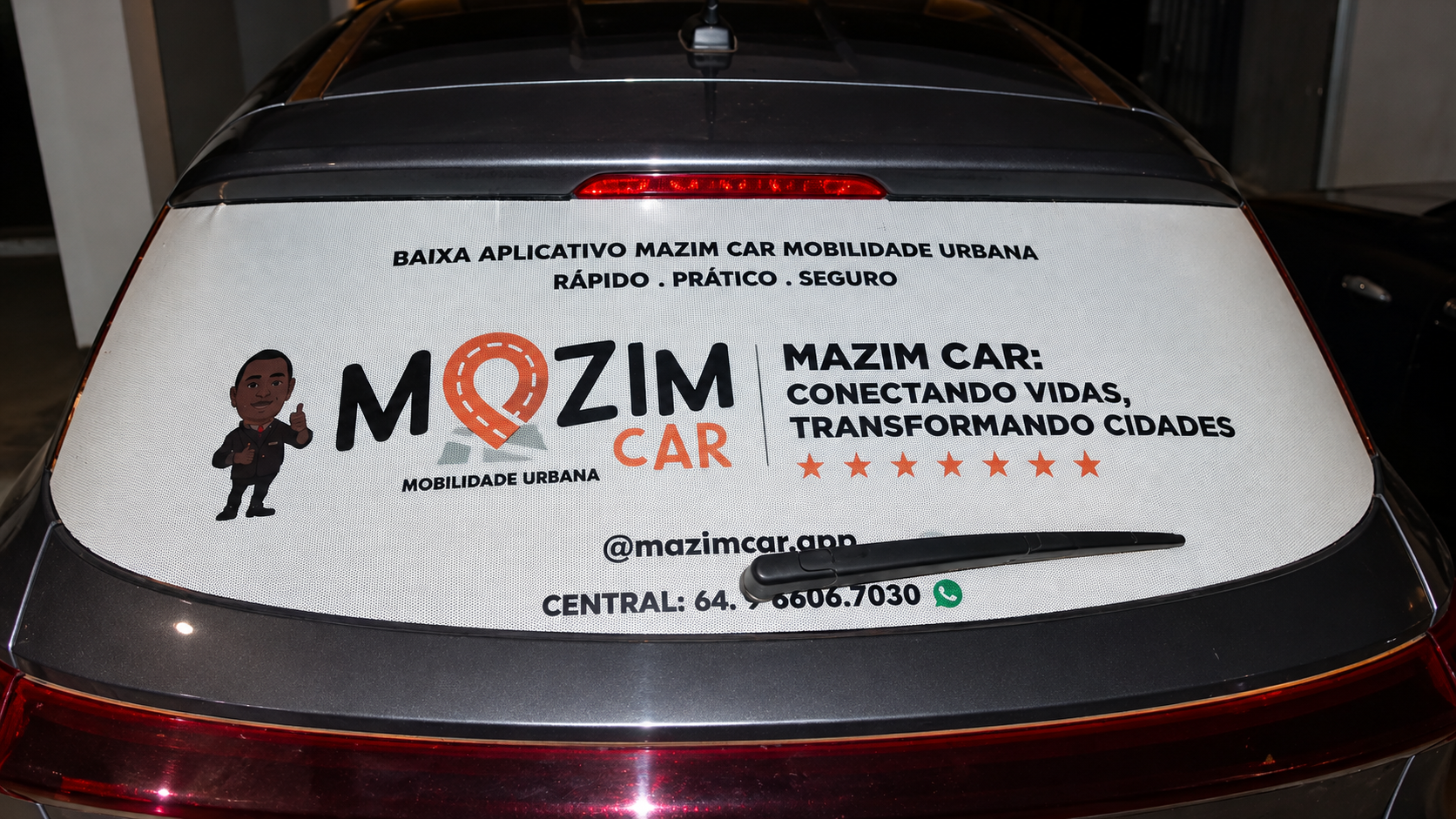 Vidro traseiro de veículo com adesivo publicitário da Mazim Car, serviço de mobilidade urbana, com logotipo, slogan e informações de contato.